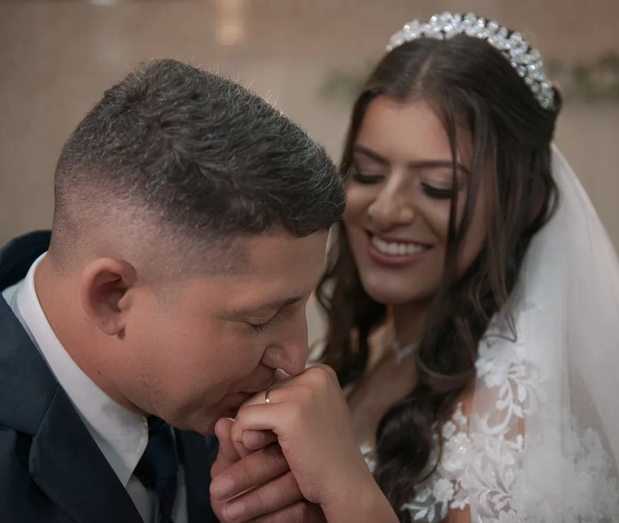 Noivo beijando a mão da noiva em momento carinhoso durante o casamento.